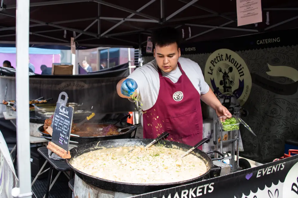 A food vendor scatters ingredients into a large pan of food.